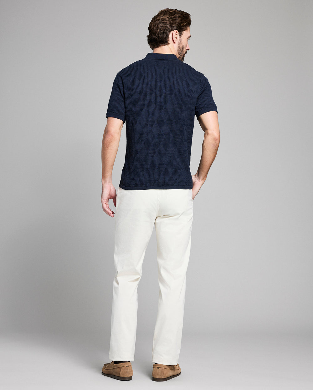 Man wearing a navy polo shirt and white pants on a gray background