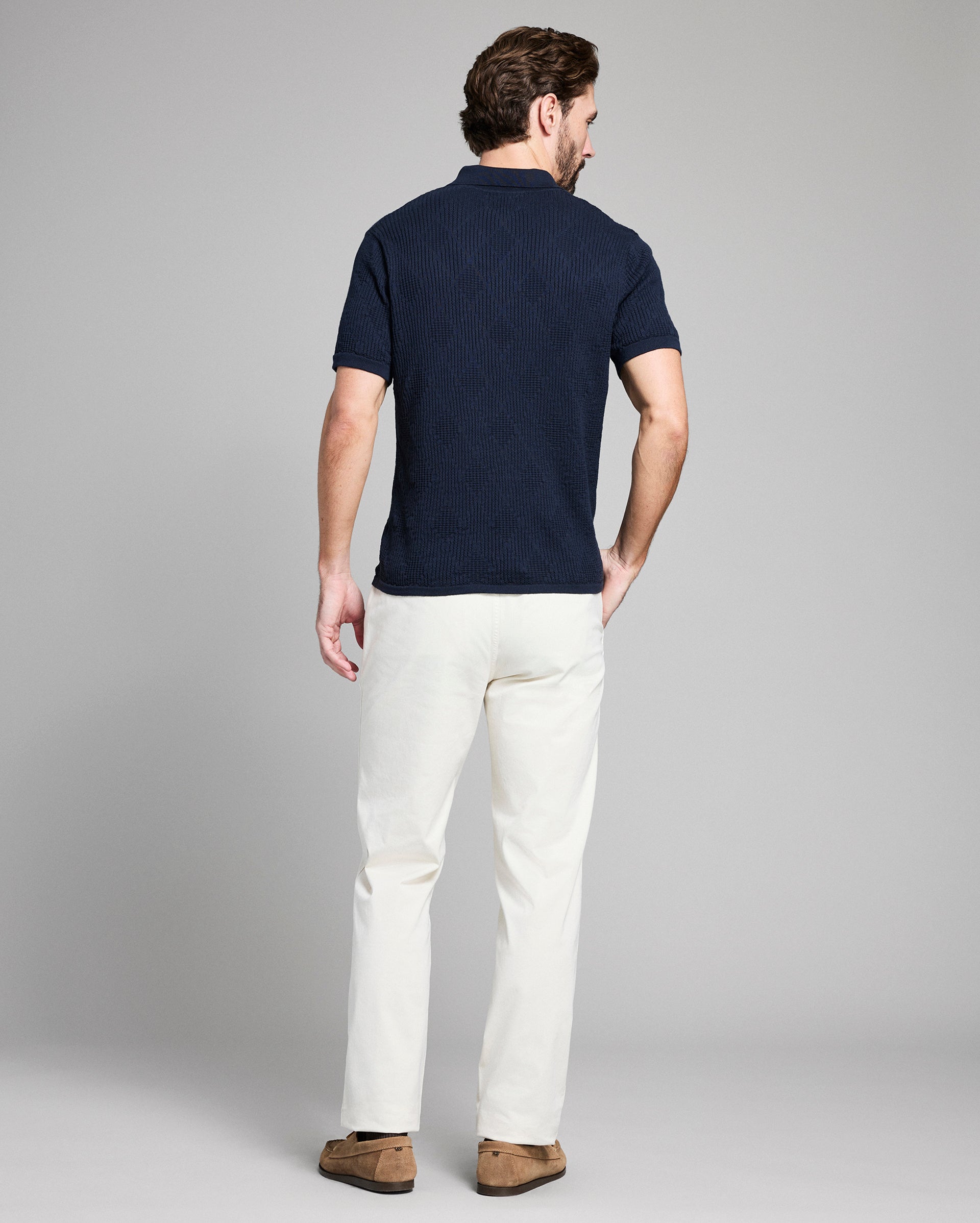 Man wearing a navy polo shirt and white pants on a gray background