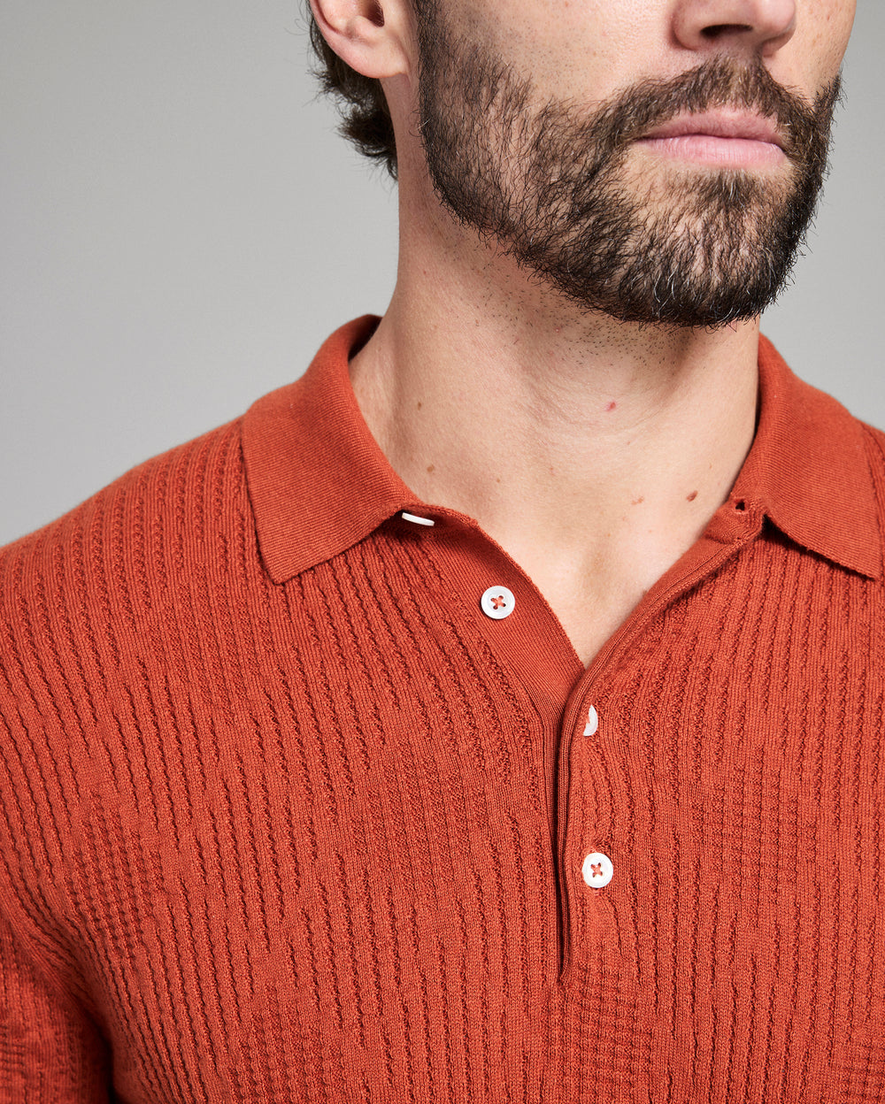 Close-up of a person wearing a rust-colored knitted polo shirt against a gray background