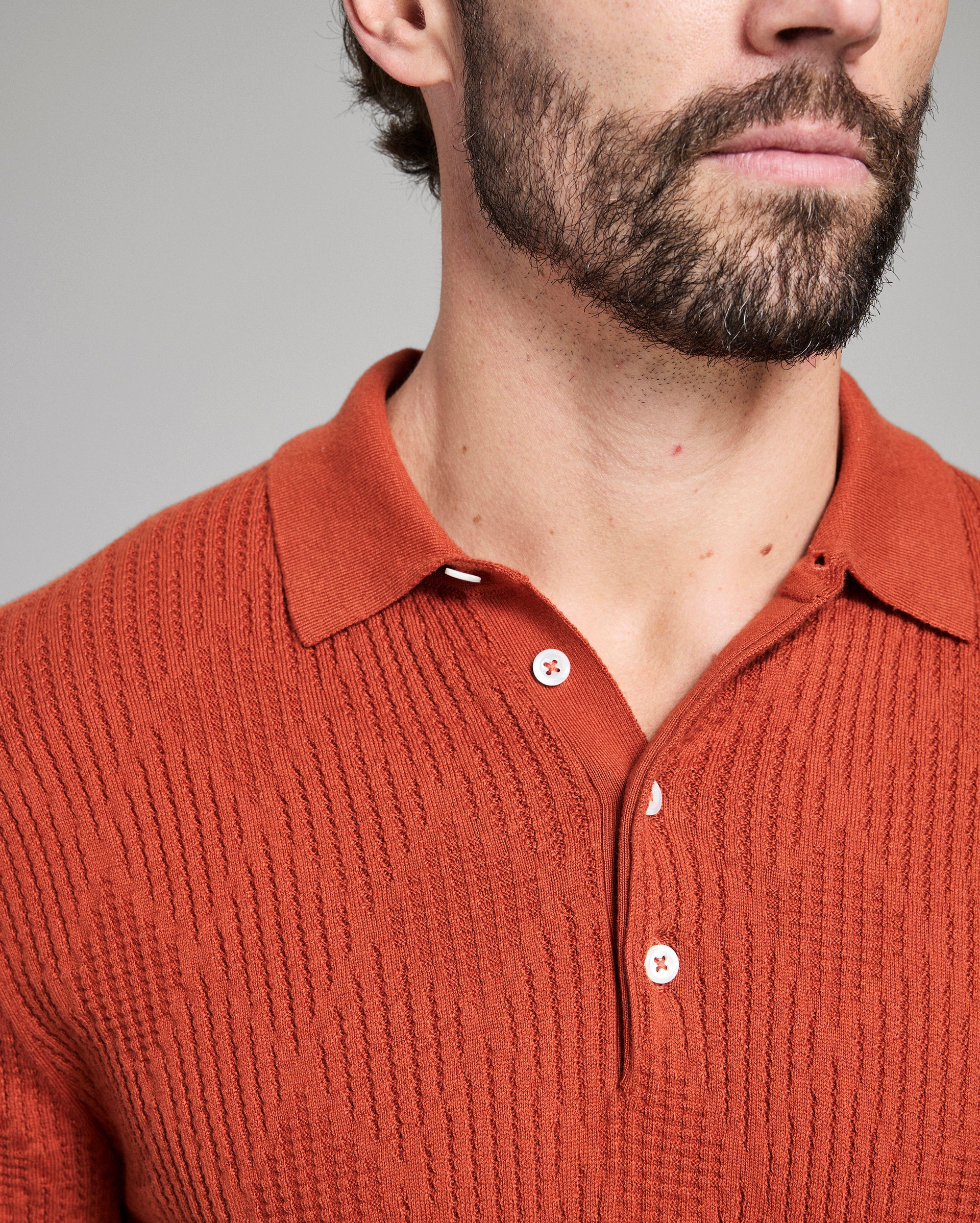 Close-up of a person wearing a rust-colored knitted polo shirt against a gray background