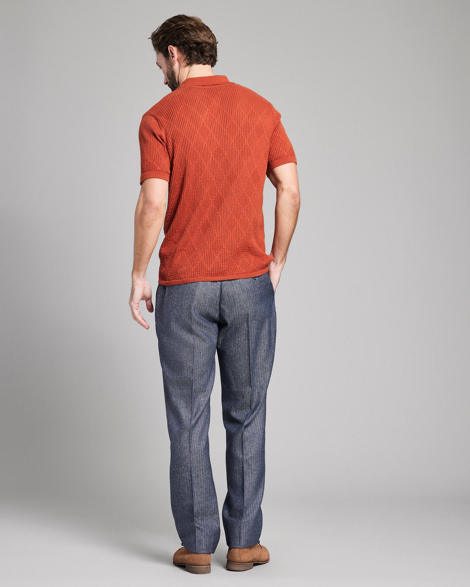 Man wearing a rust-colored polo shirt and gray pants on a plain background