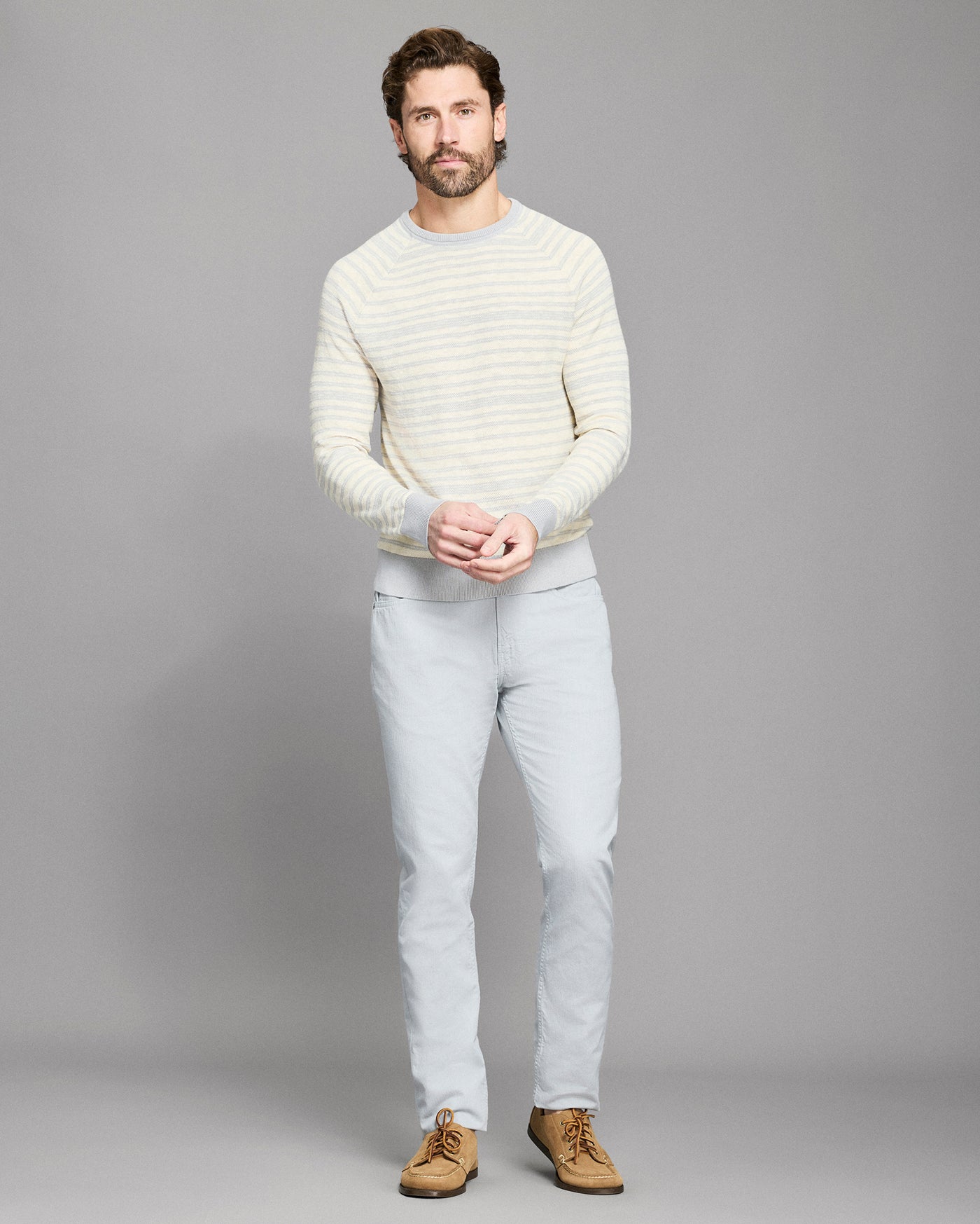 Man wearing a light-colored sweater and pants on a gray background