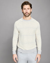 Man wearing a light-colored striped sweater and gray pants against a gray background