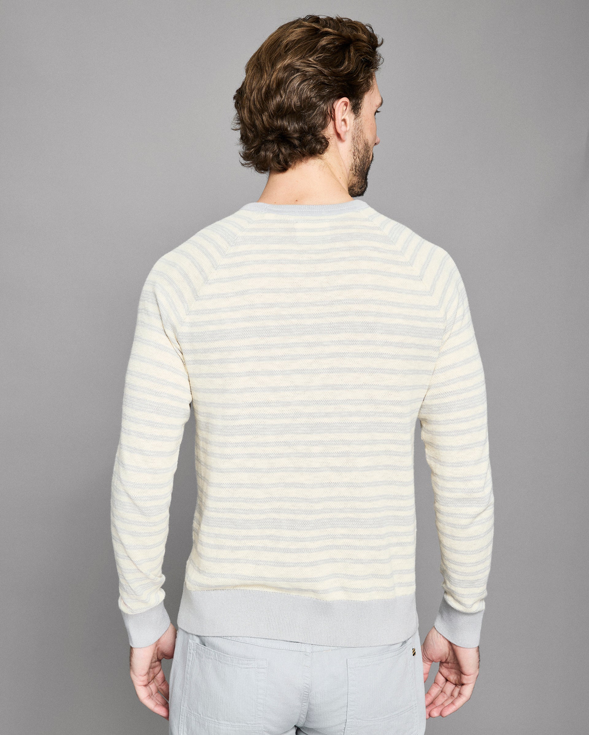 Man wearing a light-colored striped sweater against a gray background