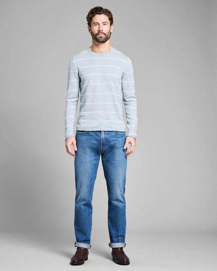 Man wearing a light blue striped sweater and blue jeans on a gray background