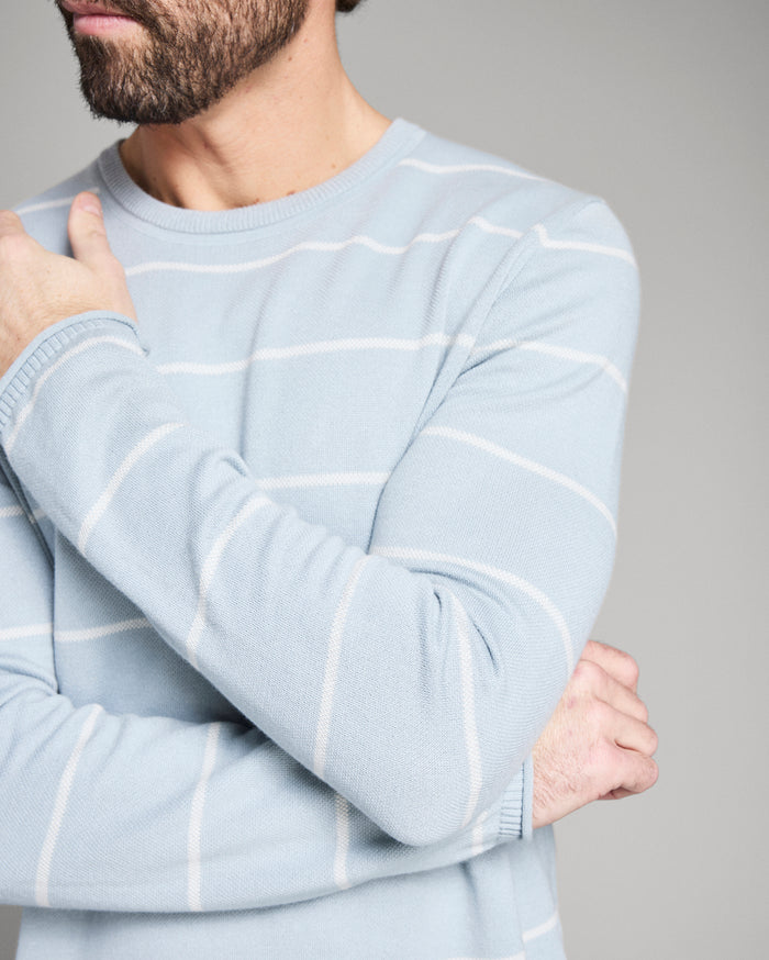 Light blue sweater with white stripes worn by a person on a gray background