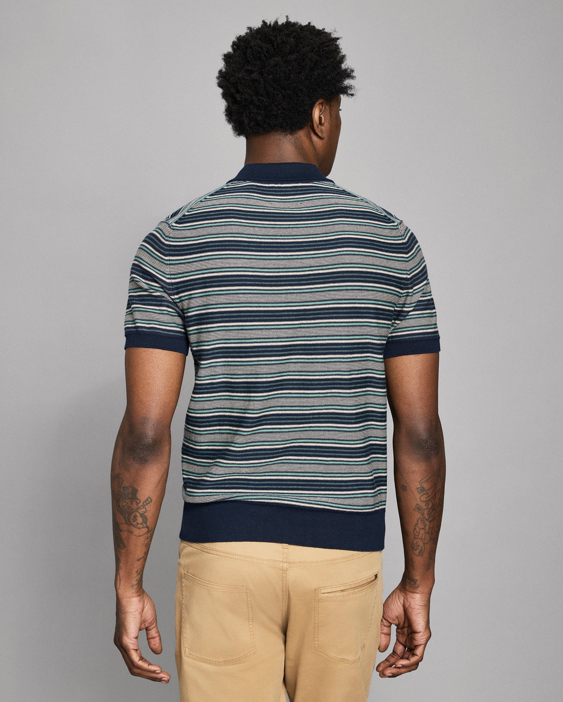 Man wearing a striped polo shirt and beige pants against a gray background