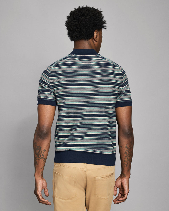 Man wearing a striped polo shirt and beige pants against a gray background
