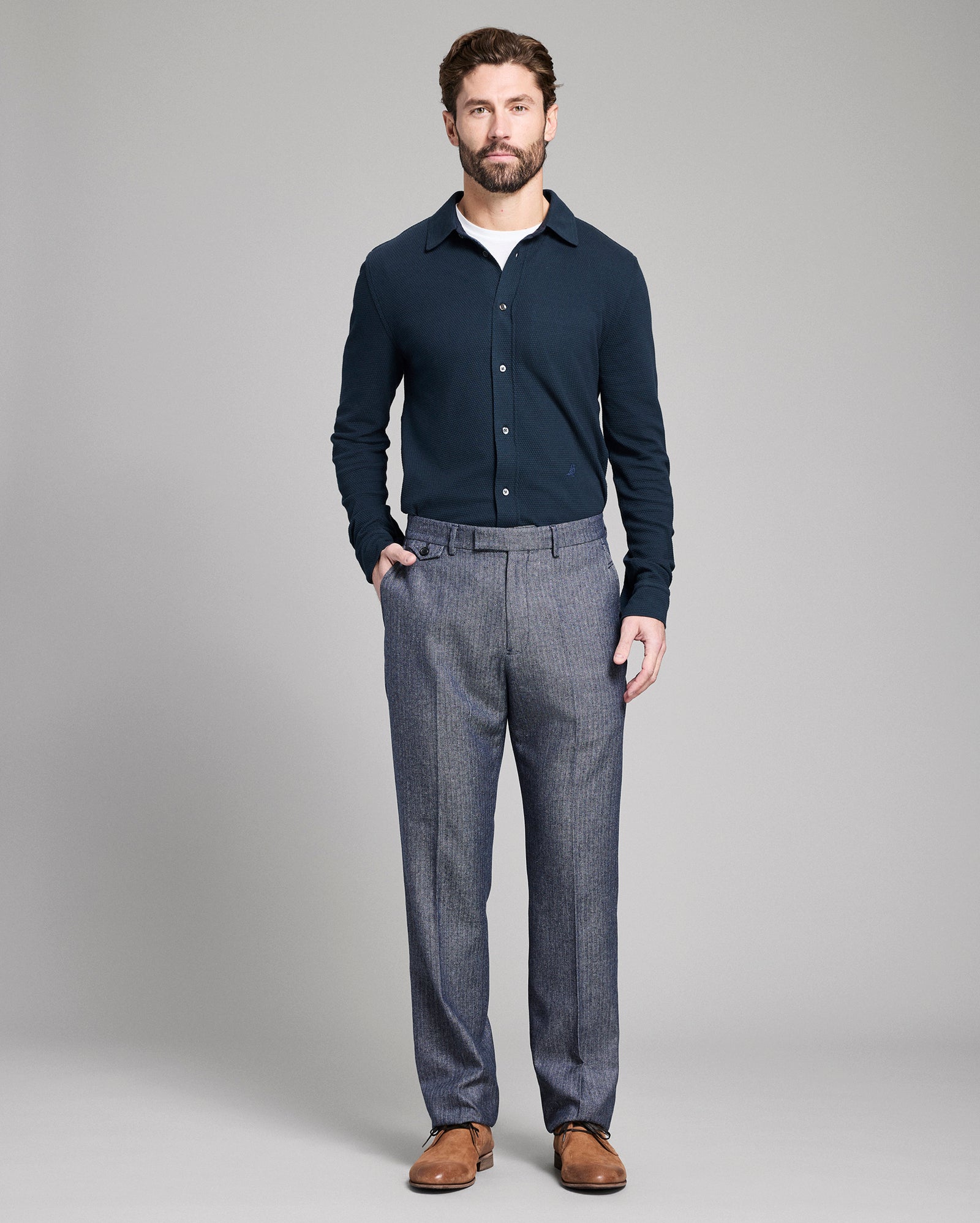 Man wearing a navy sweater and gray pants on a gray background