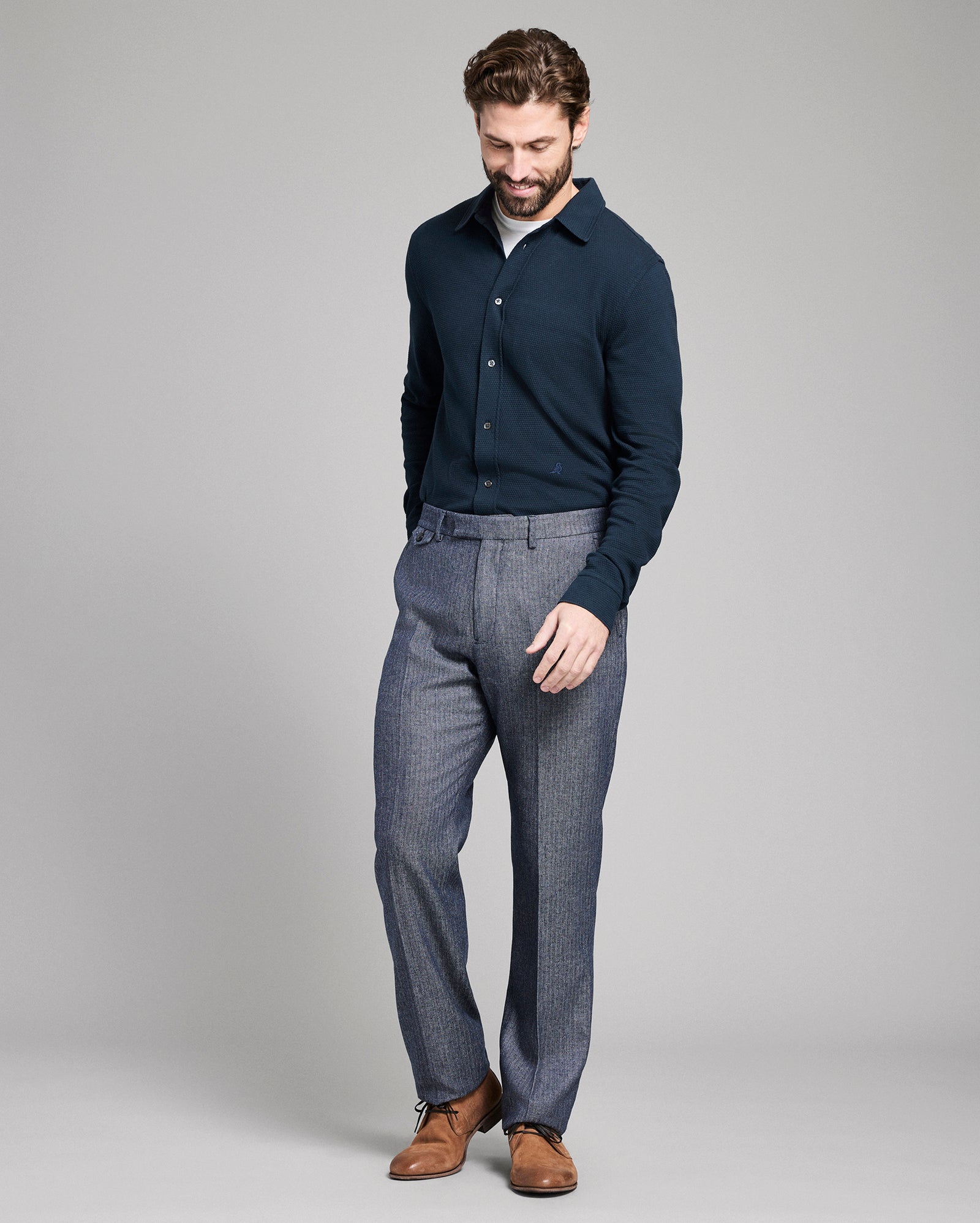 Man wearing a navy sweater and gray pants on a gray background