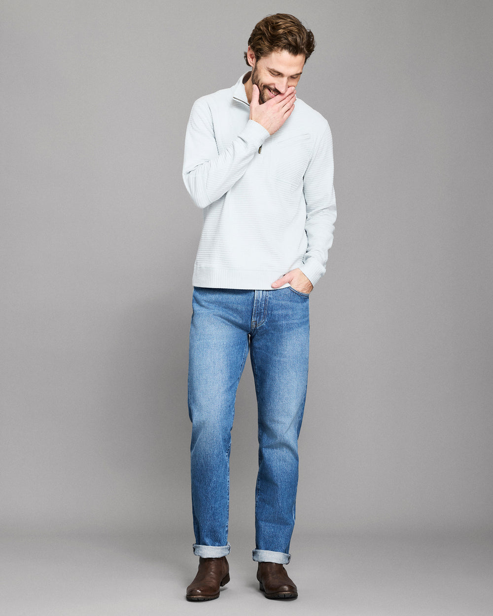 Man wearing a light gray sweater and blue jeans on a gray background