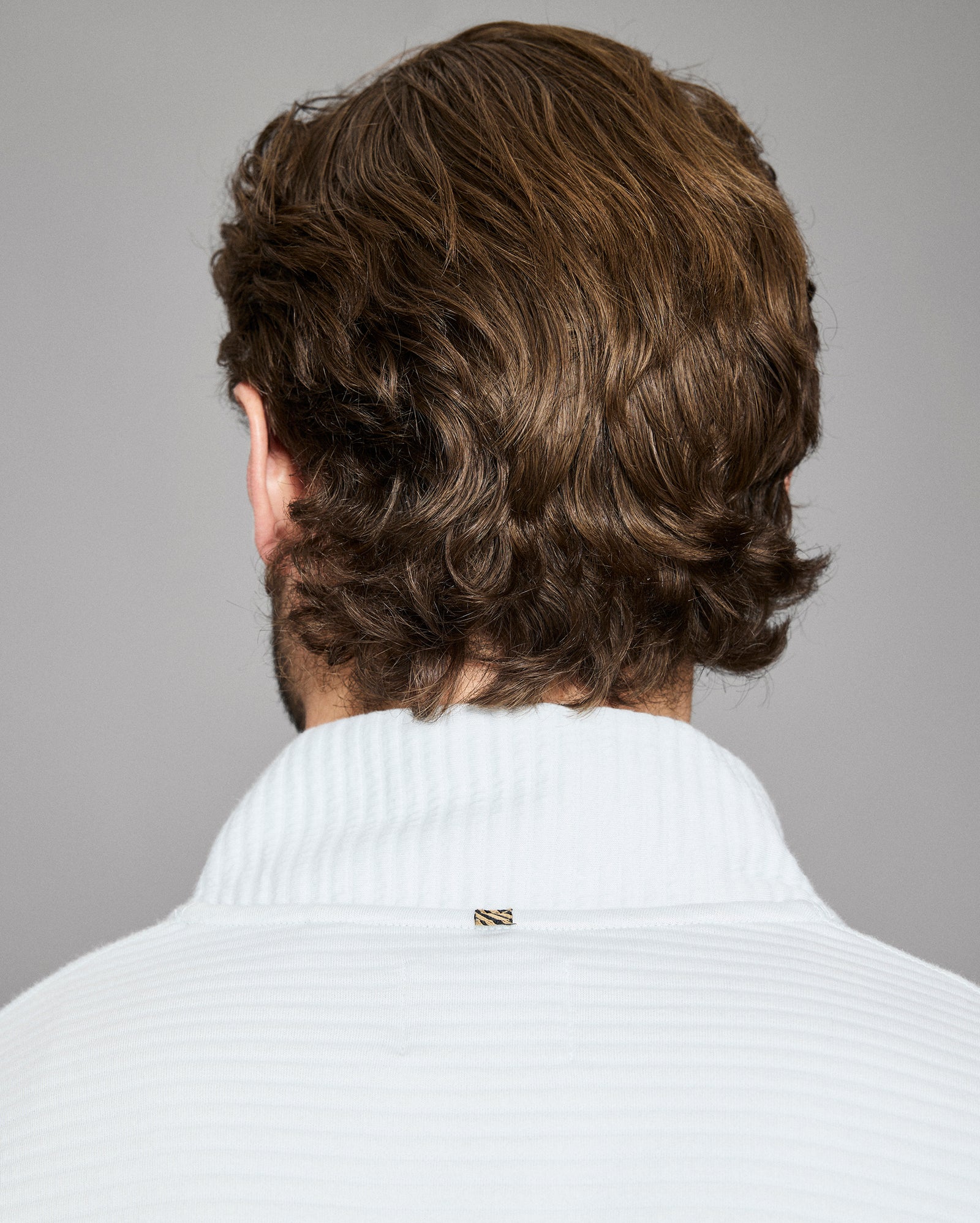 Man with wavy brown hair wearing a white sweater against a gray background