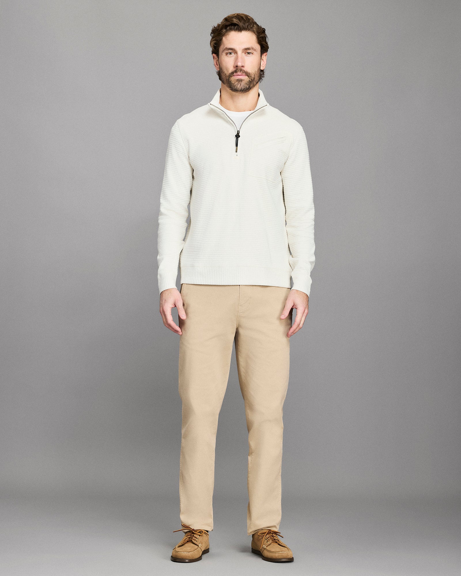 Man wearing a white sweater and beige pants against a gray background