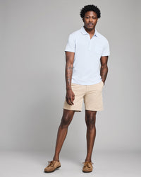 Man wearing a white polo shirt and beige shorts against a gray background