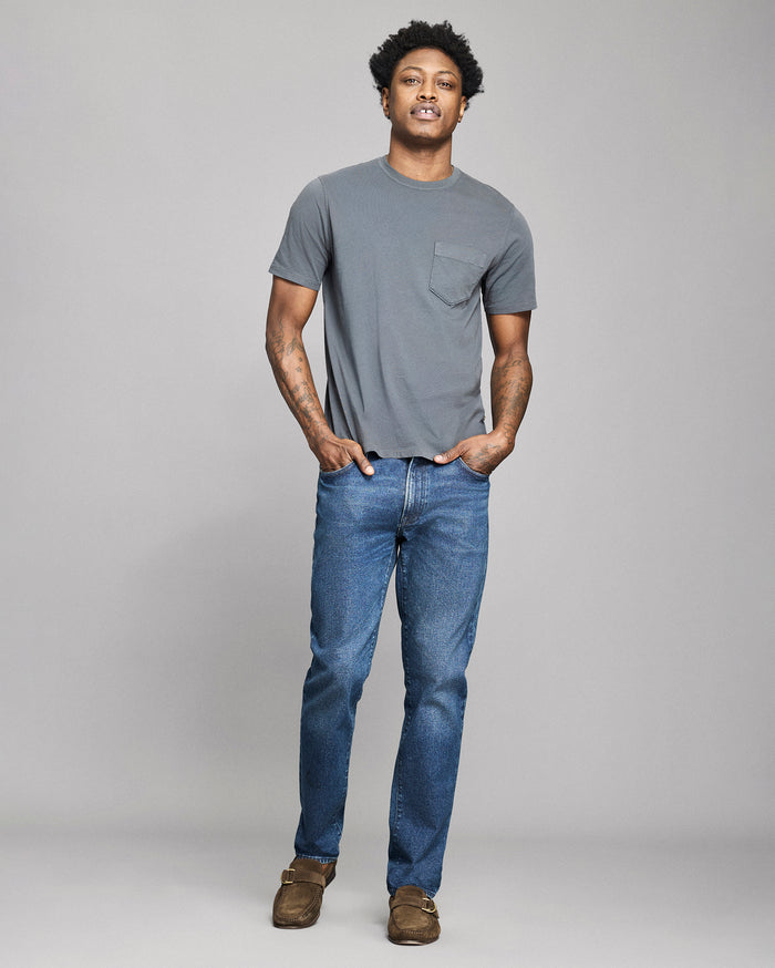 Man wearing a gray t-shirt and blue jeans against a plain background