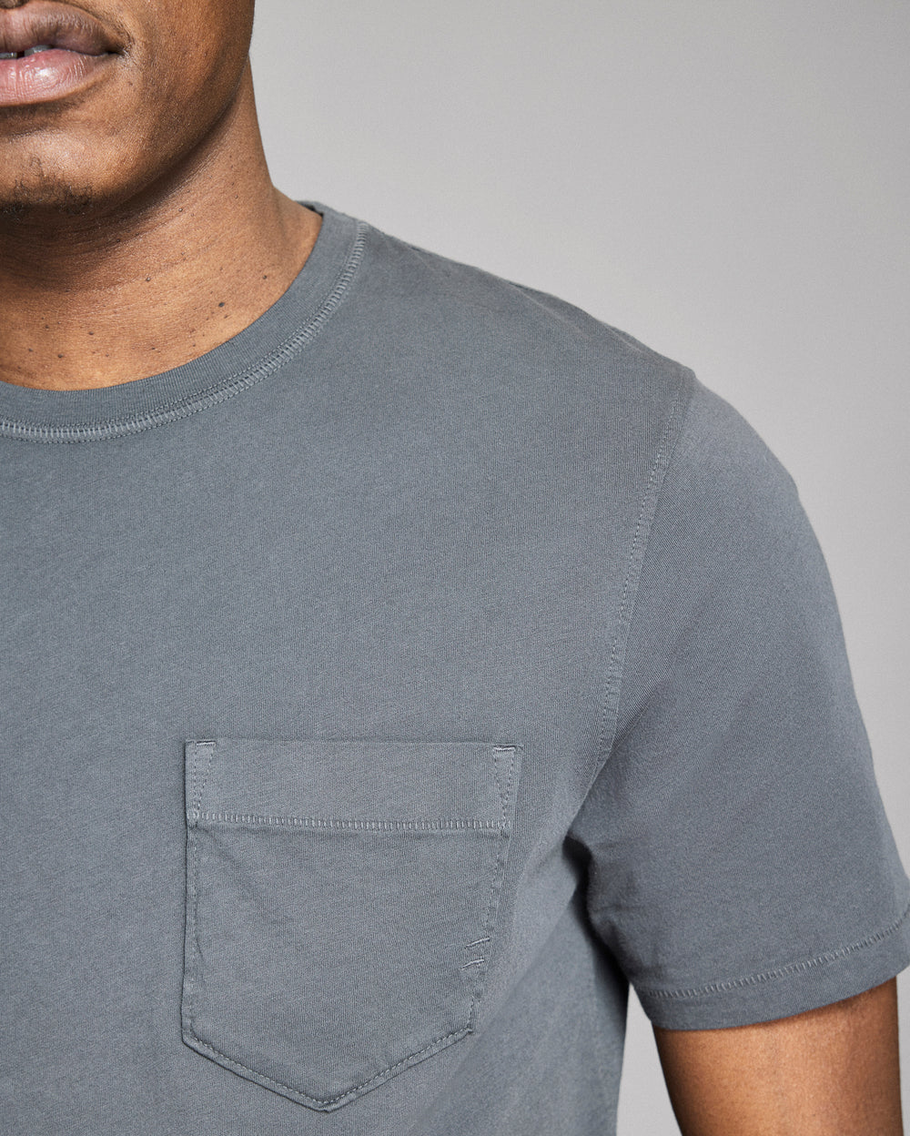 Man wearing a gray t-shirt with a pocket on a plain background