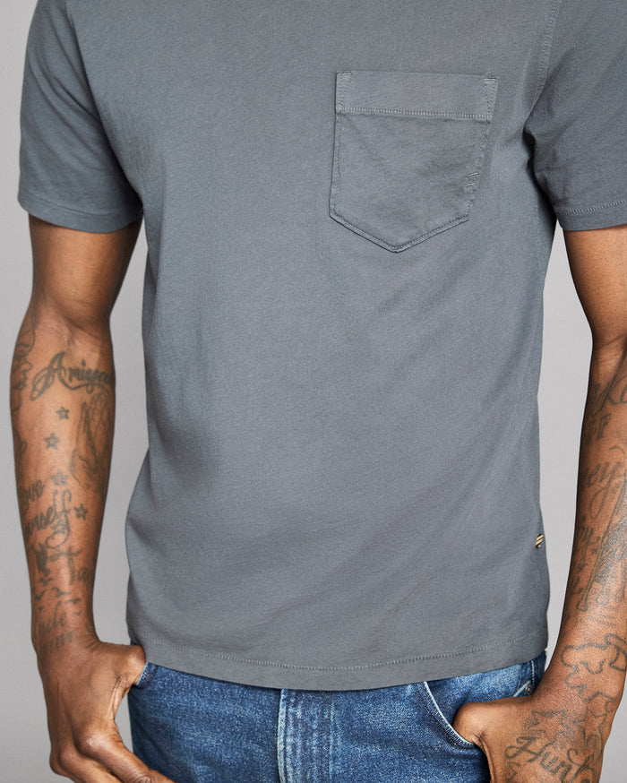 Gray t-shirt with a pocket worn by a person with tattoos on a plain background
