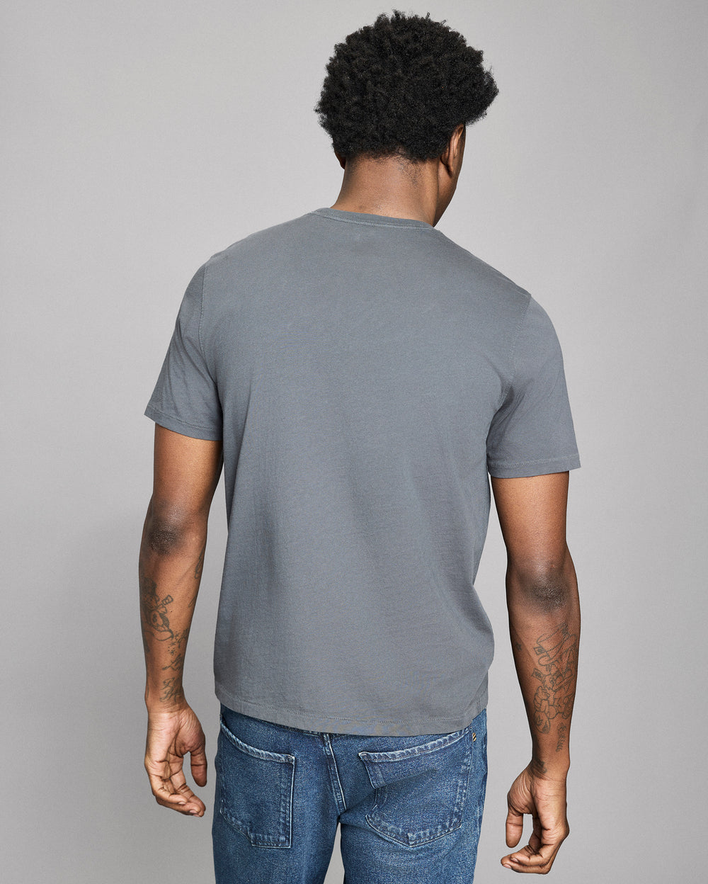 Man wearing a gray t-shirt and blue jeans against a plain background