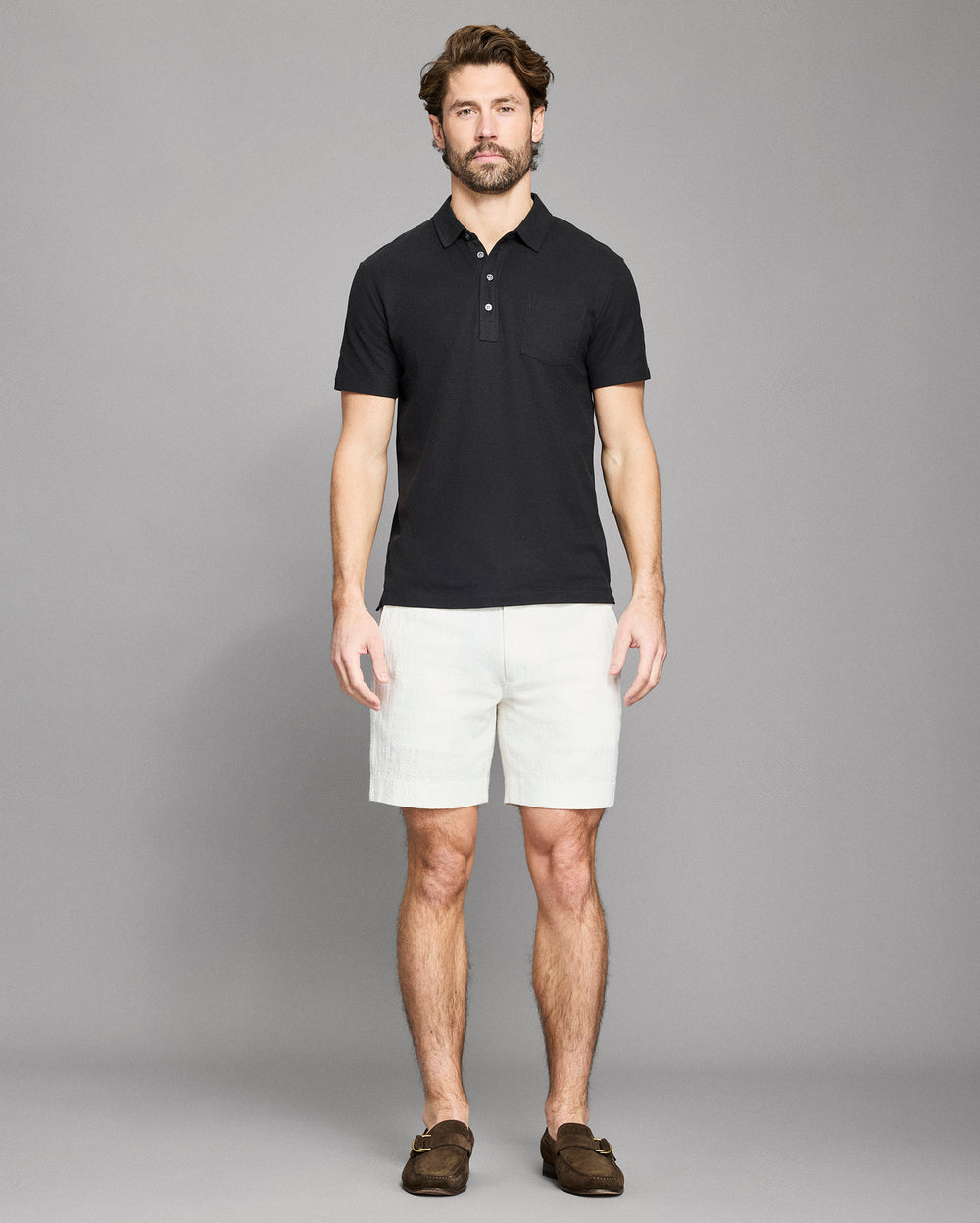 Man wearing a black polo shirt and white shorts against a gray background
