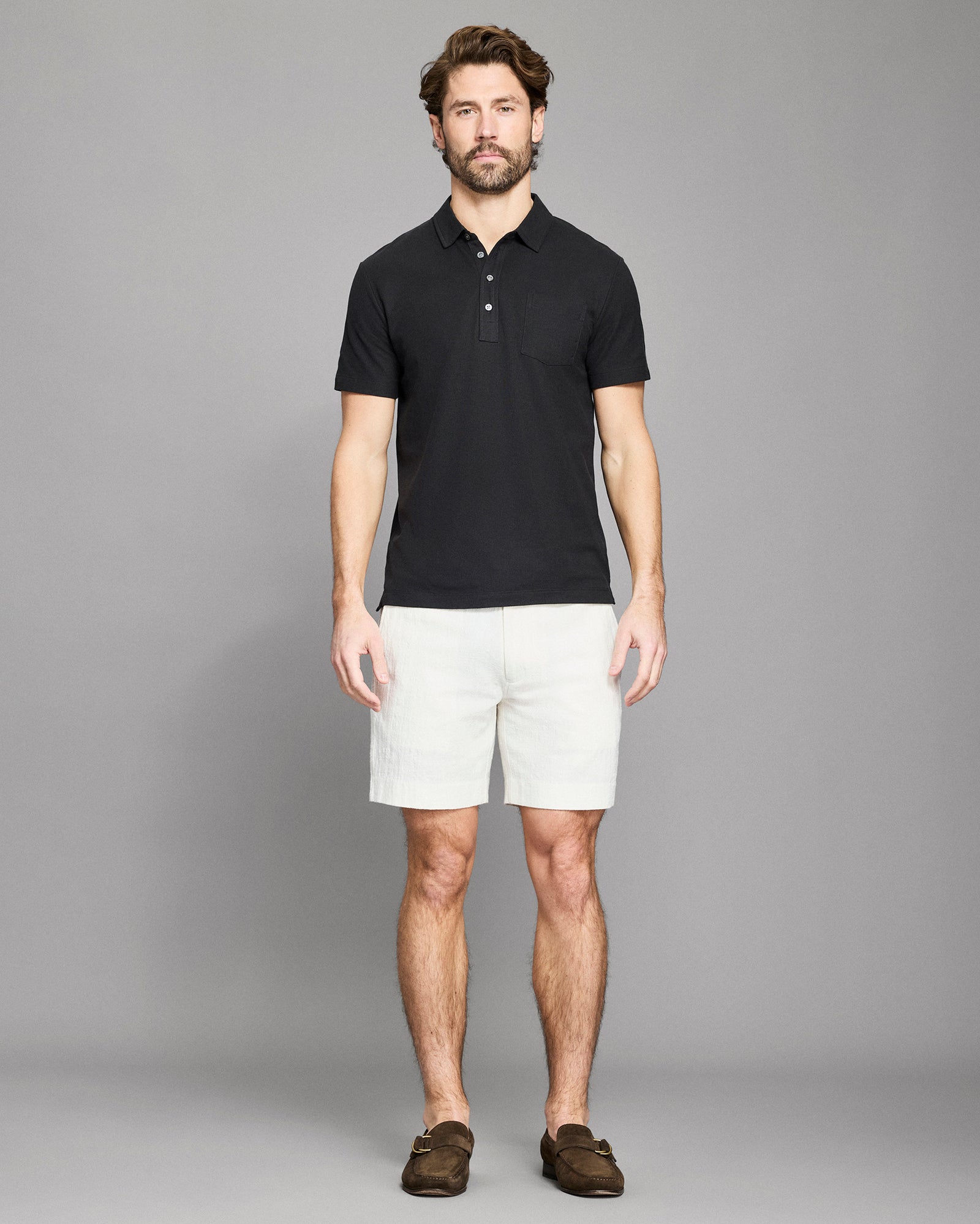 Man wearing a black polo shirt and white shorts against a gray background