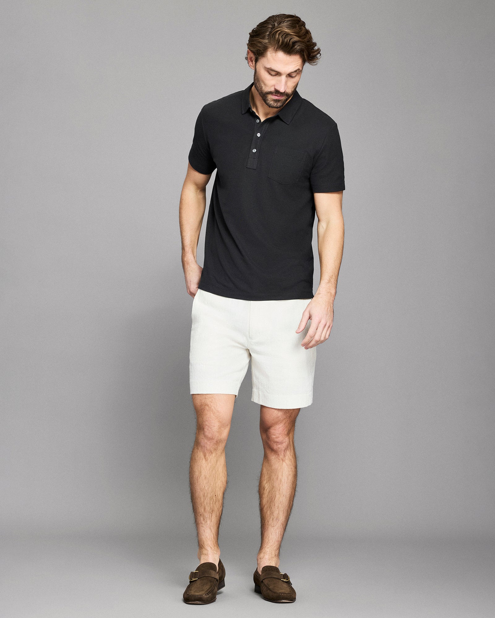 Man wearing a black polo shirt and white shorts against a gray background