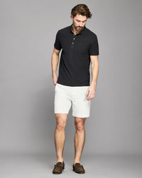Man wearing a black polo shirt and white shorts against a gray background