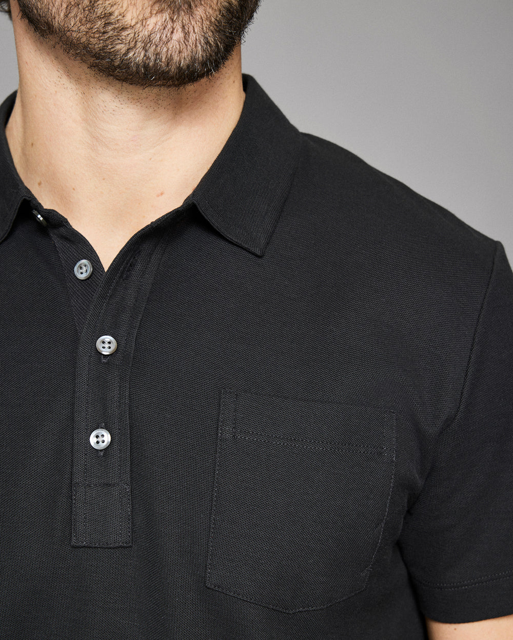 Close-up of a black polo shirt with buttons on a gray background