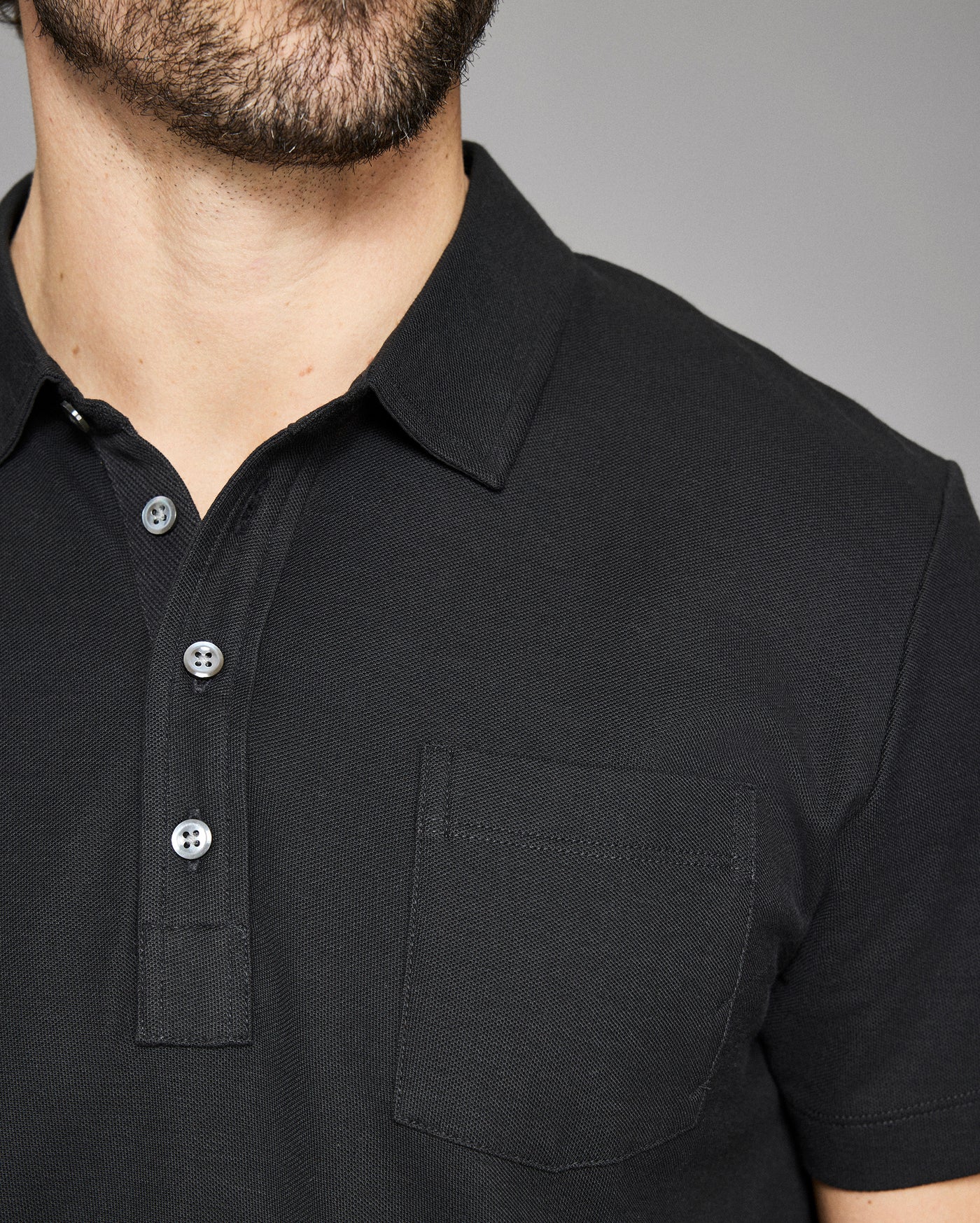 Close-up of a black polo shirt with buttons on a gray background