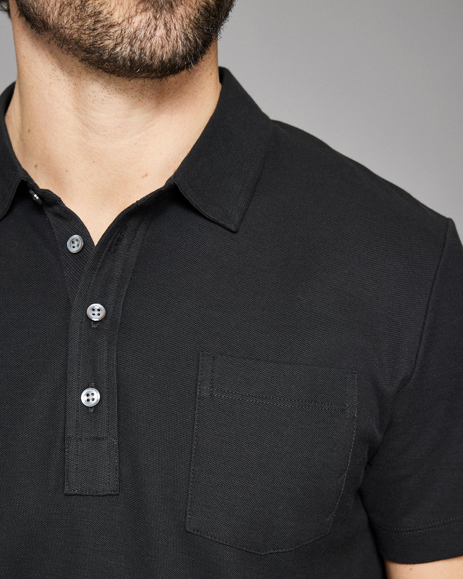 Close-up of a black polo shirt with buttons on a gray background