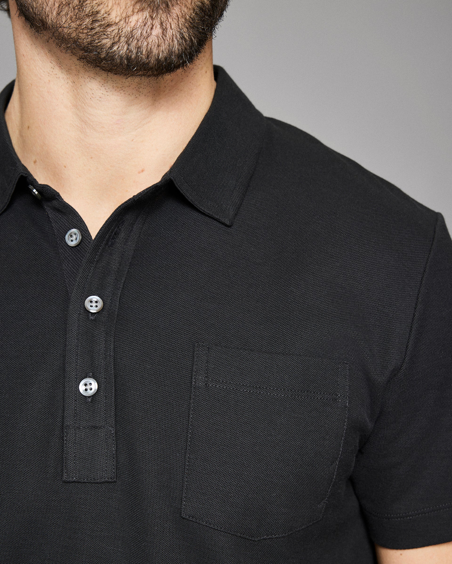 Close-up of a black polo shirt with buttons on a gray background