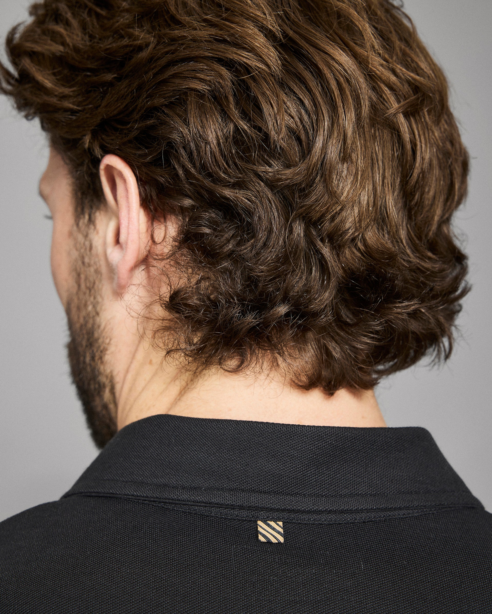 Man with styled hair wearing a black shirt against a gray background
