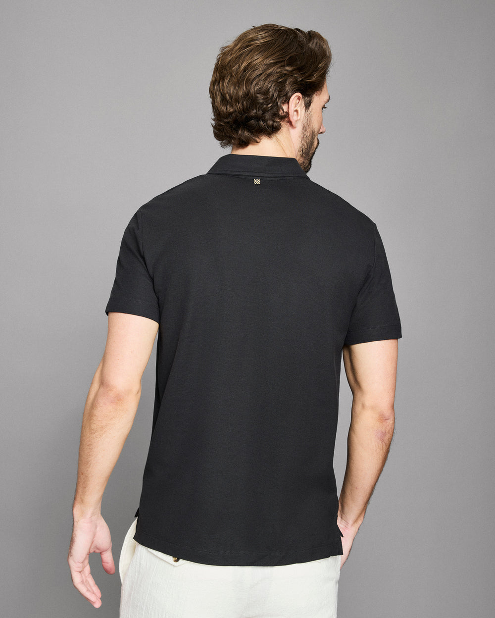 Man wearing a black polo shirt against a gray background
