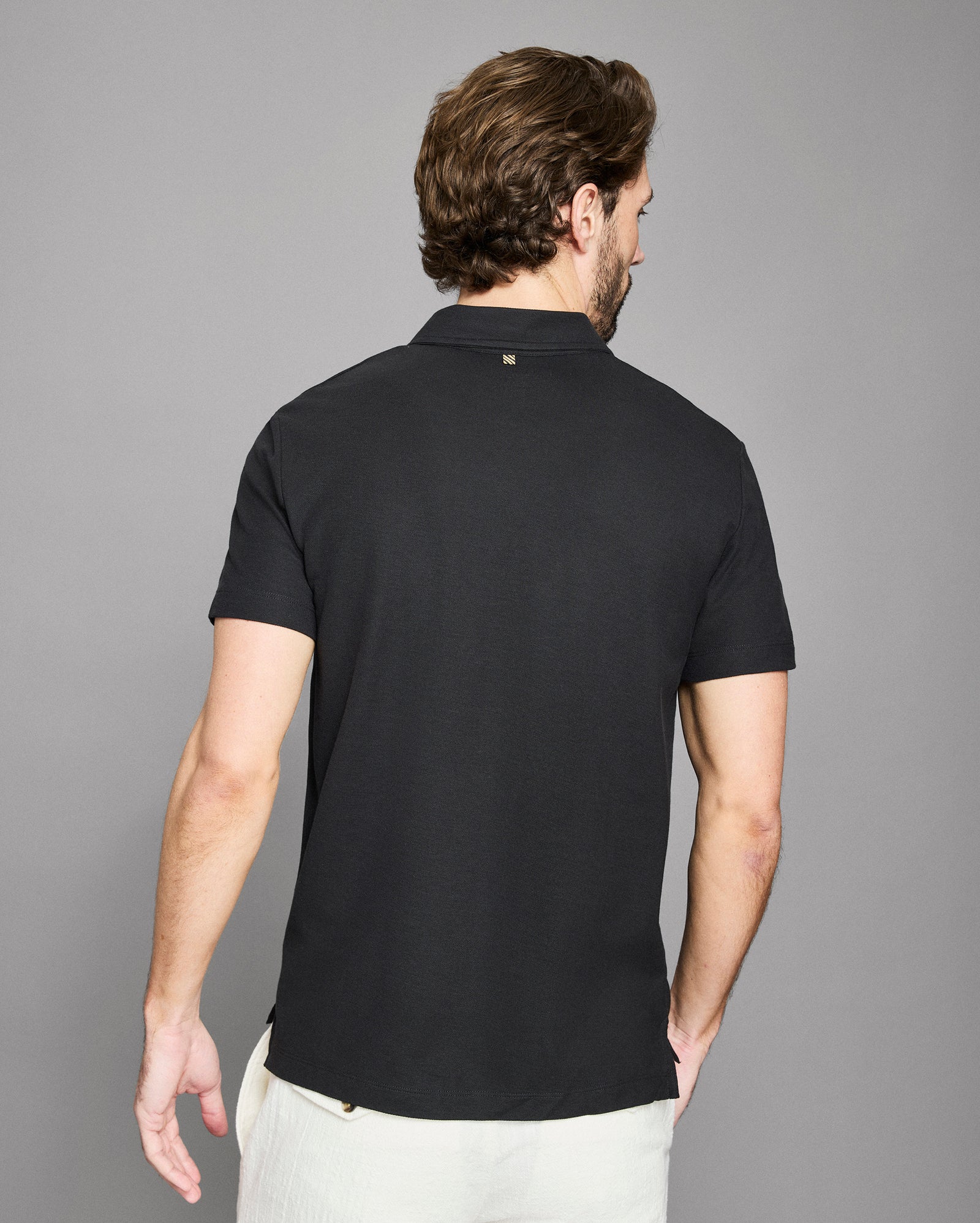 Man wearing a black polo shirt against a gray background