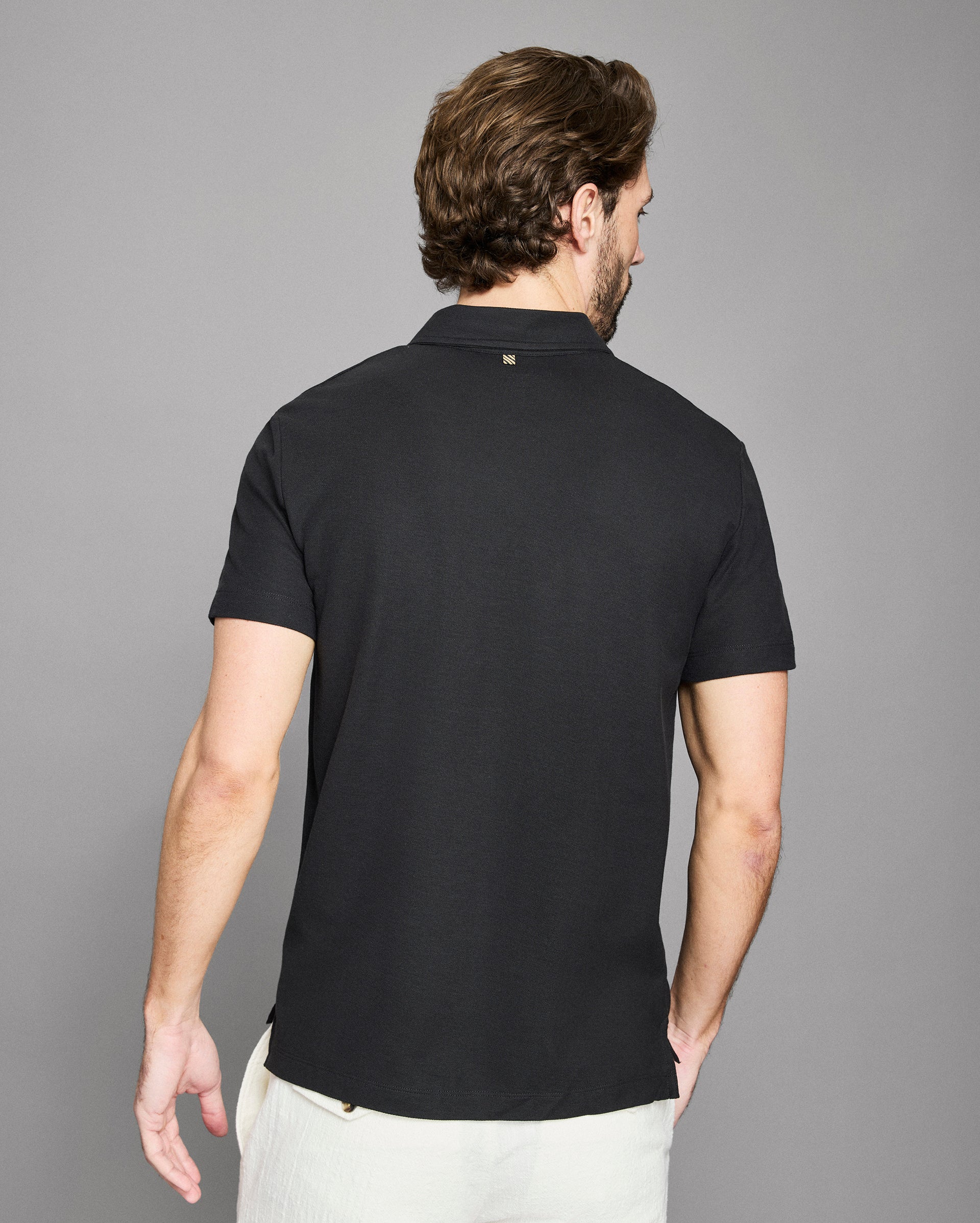 Man wearing a black polo shirt against a gray background
