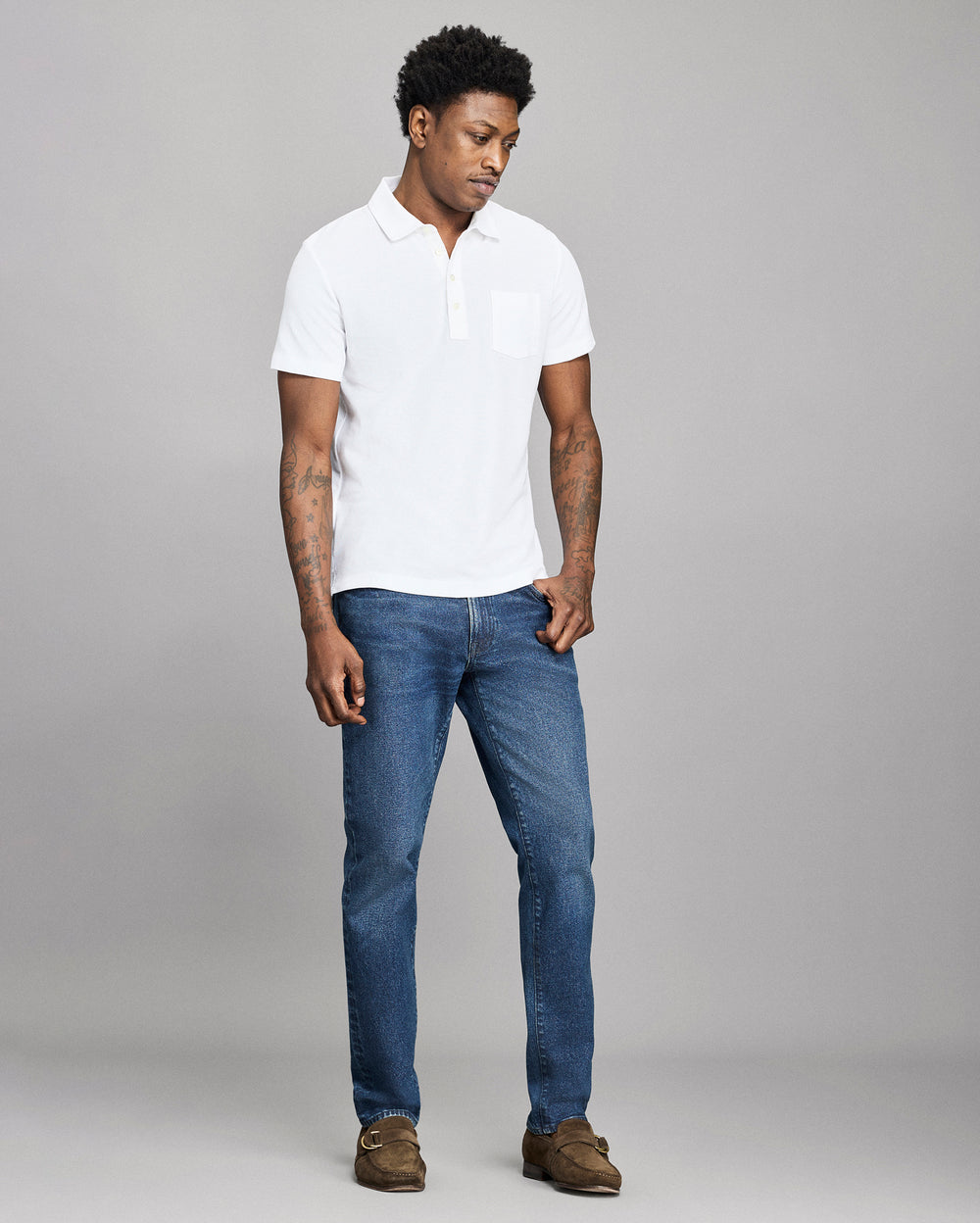 Man wearing a white polo shirt and blue jeans against a gray background