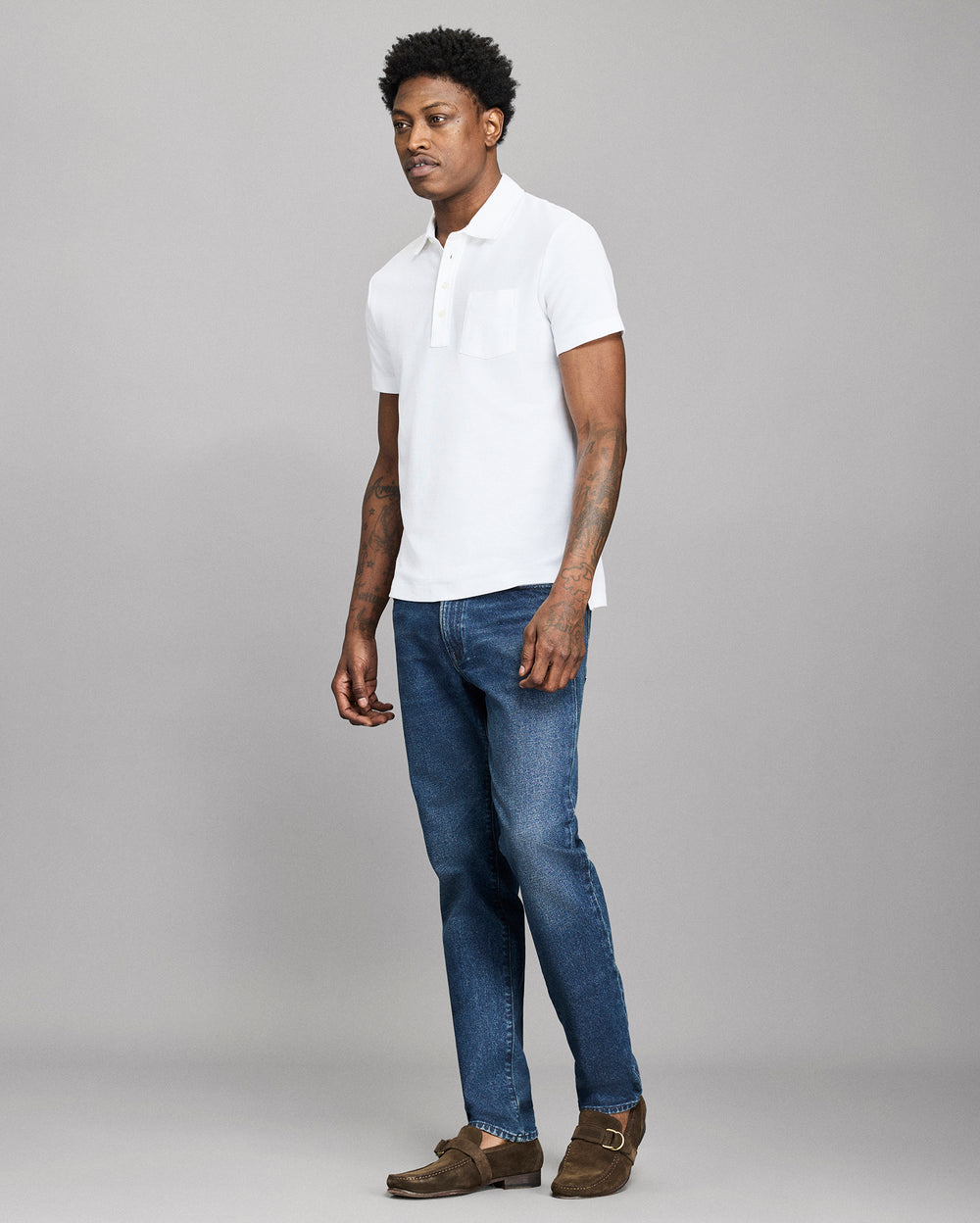 Man wearing a white polo shirt and blue jeans on a gray background
