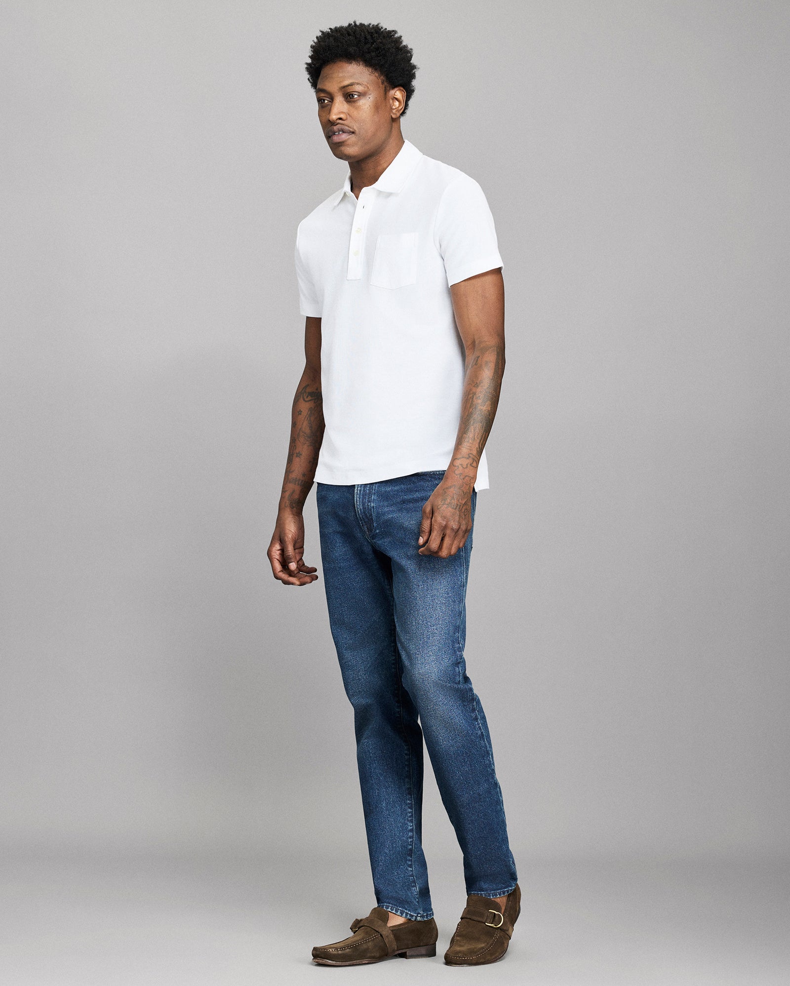 Man wearing a white polo shirt and blue jeans on a gray background