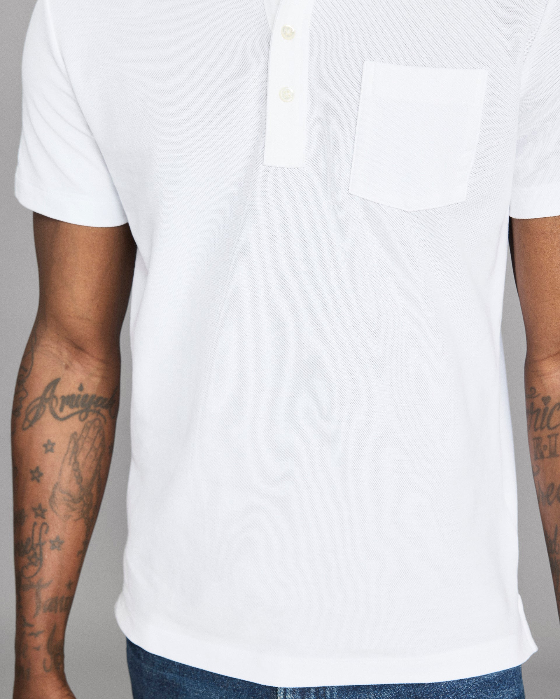 White polo shirt worn by a person with tattoos on arms against a gray background