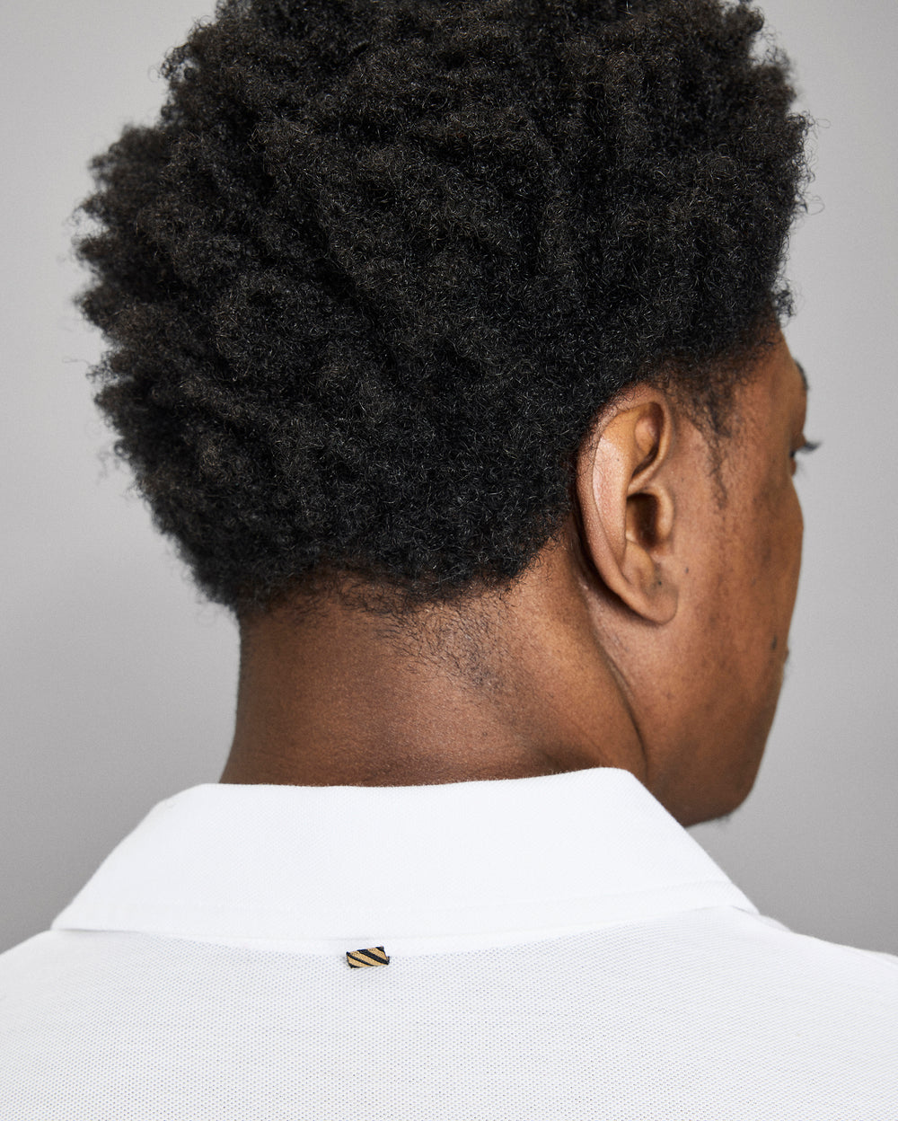 Person wearing a white shirt with a gold button on a gray background