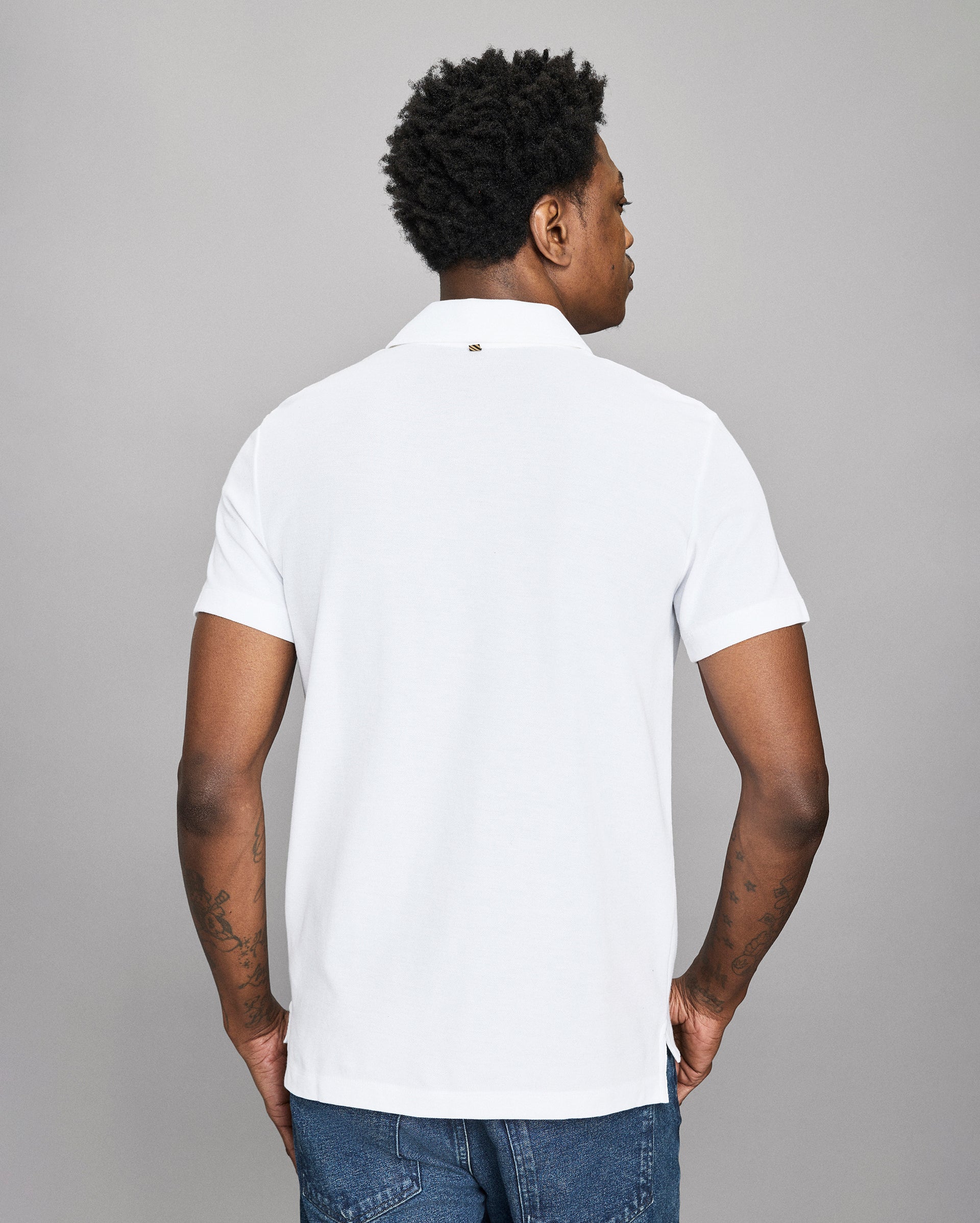 Man wearing a white polo shirt and blue jeans against a gray background