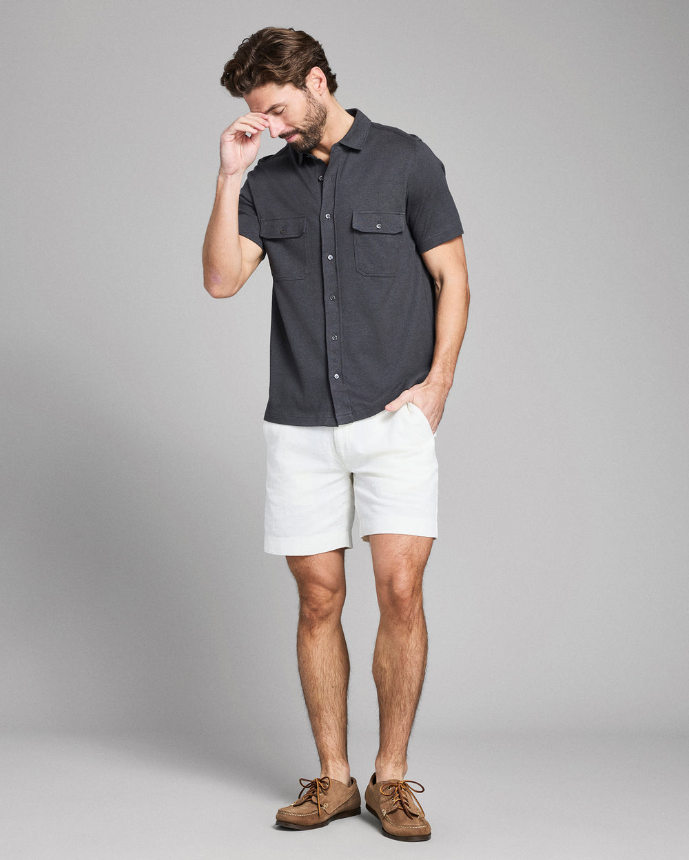 Man wearing a dark gray short-sleeve shirt and white shorts on a gray background