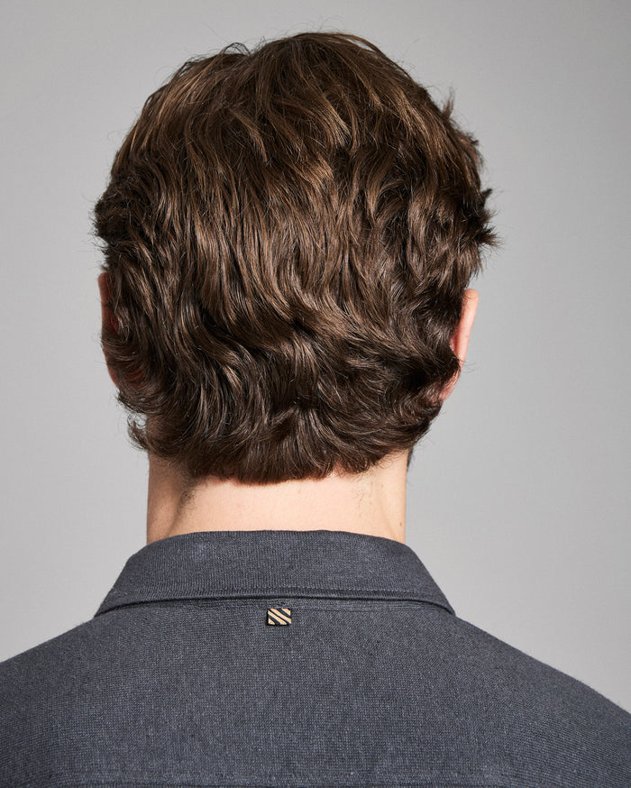 Back view of a person with styled hair wearing a gray shirt against a gray background