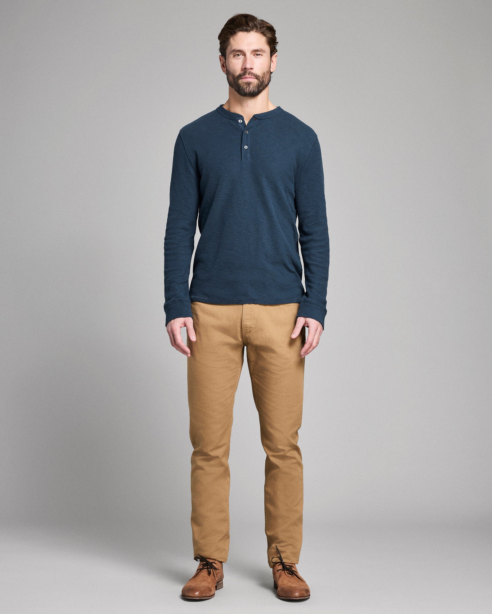 Man wearing a blue long-sleeve shirt and tan pants on a gray background