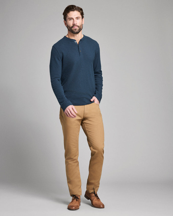 Man wearing a navy blue henley shirt and tan pants on a gray background