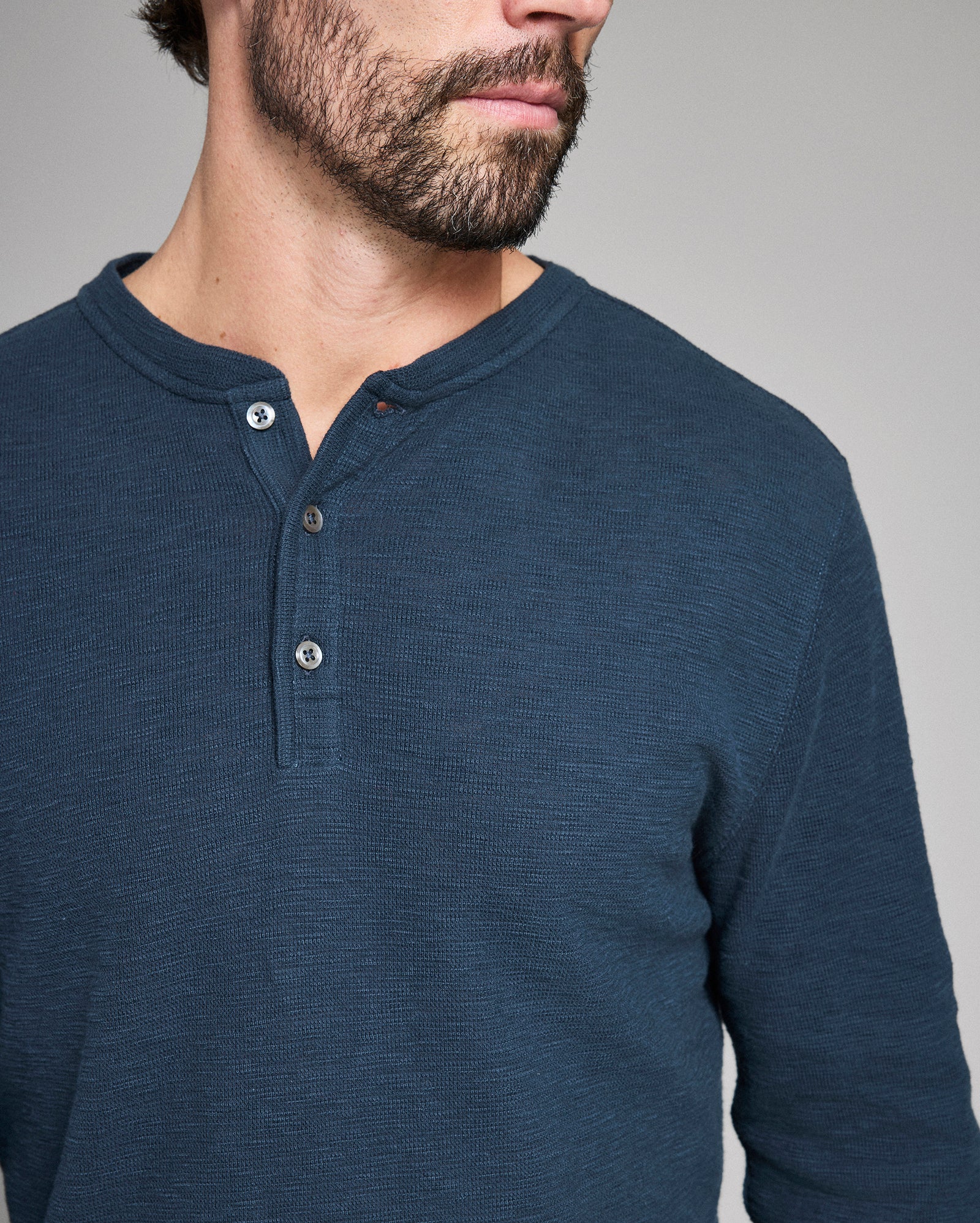 Man wearing a blue henley shirt against a gray background