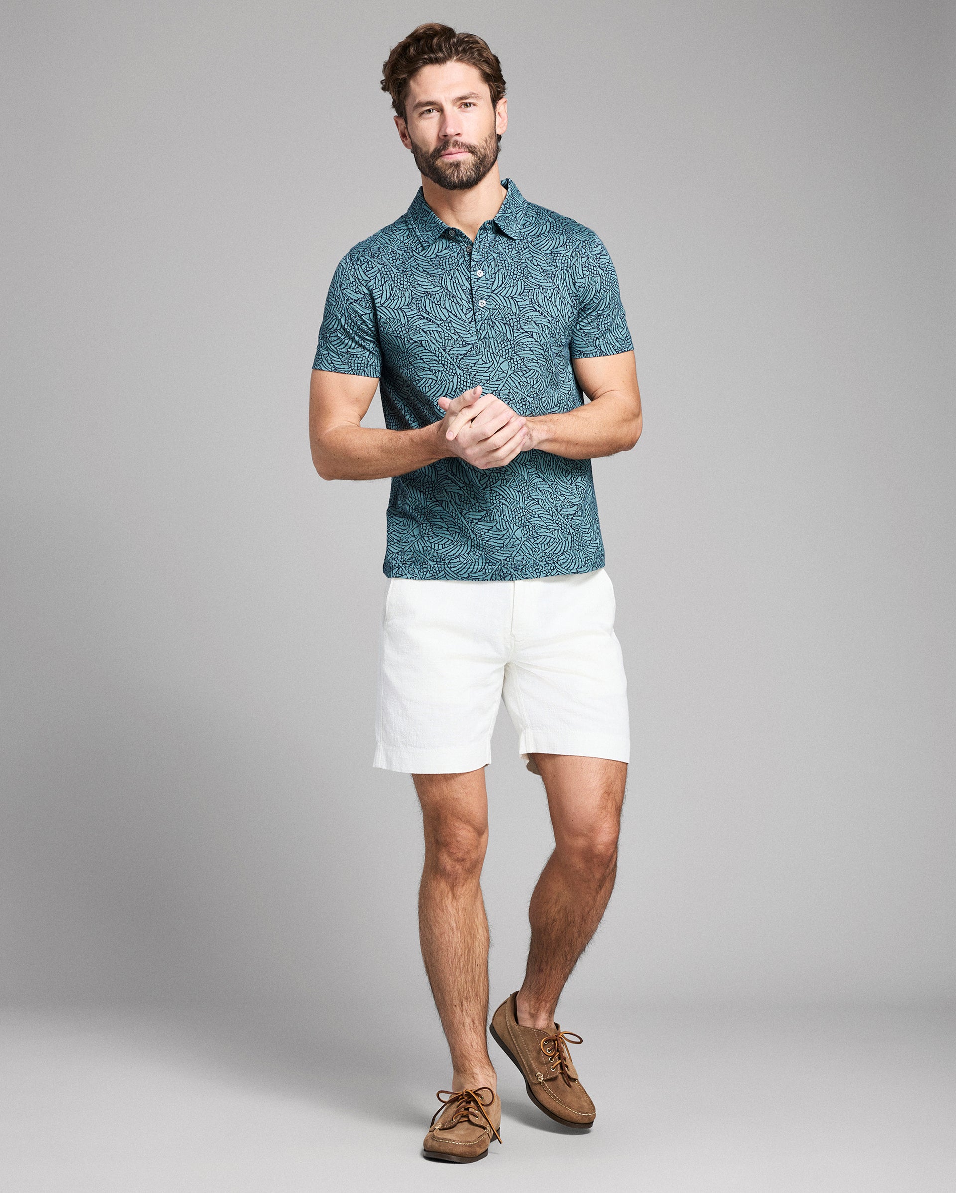Man wearing a blue patterned polo shirt and white shorts on a gray background