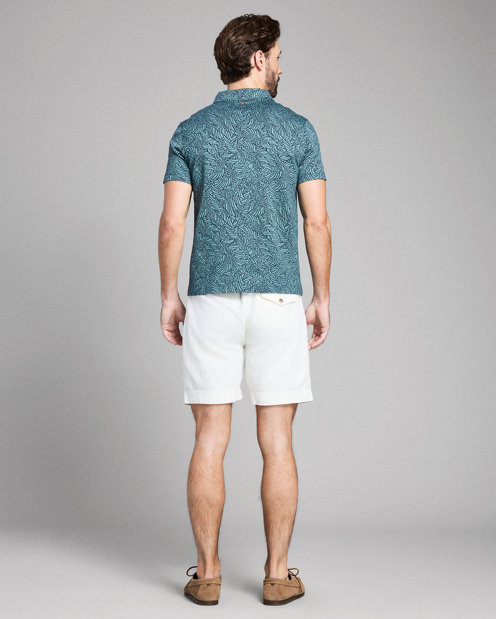 Man wearing a blue patterned shirt and white shorts on a gray background