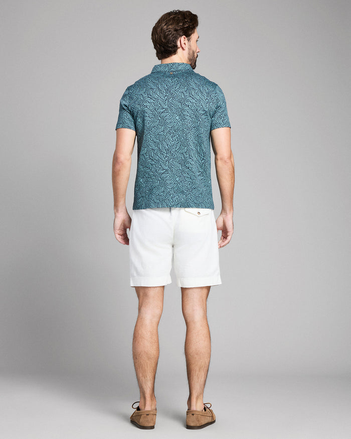 Man wearing a blue patterned shirt and white shorts on a gray background