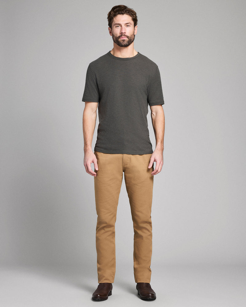 Man wearing a dark gray t-shirt and tan pants on a gray background Alternate