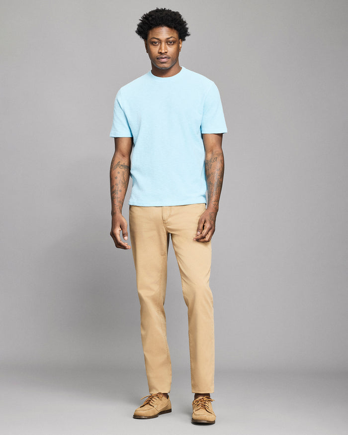Man wearing a light blue t-shirt and beige pants against a gray background
